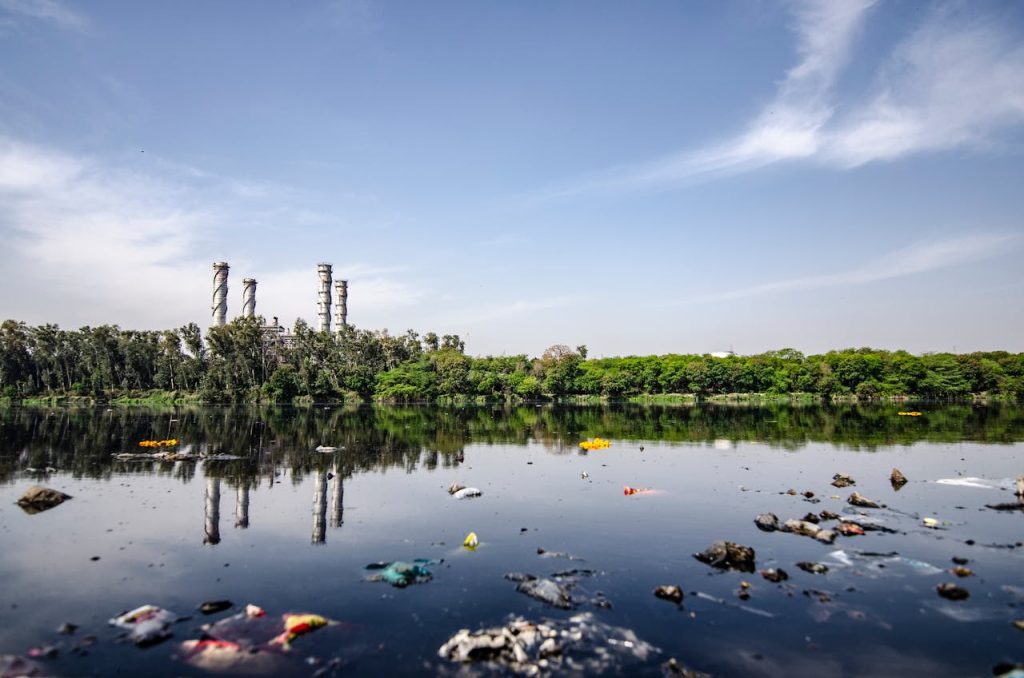 A polluted river reflecting industrial structures and surrounded by litter.