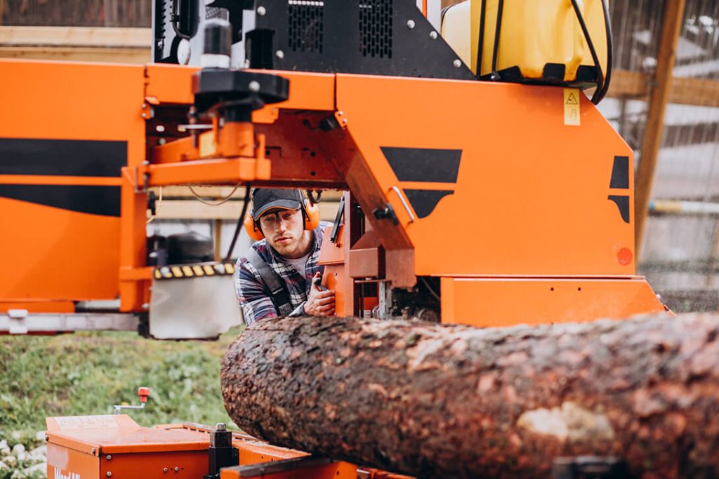 A lumberjack operating a sawmill with a large log in focus.